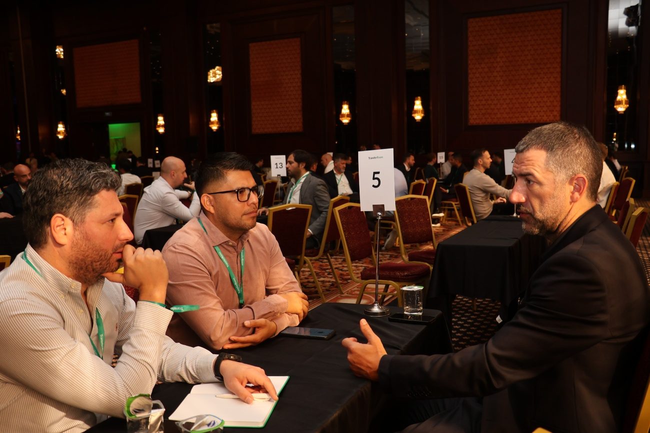 Two agents listening to a man speaking across a numbered meeting table in a large event hall